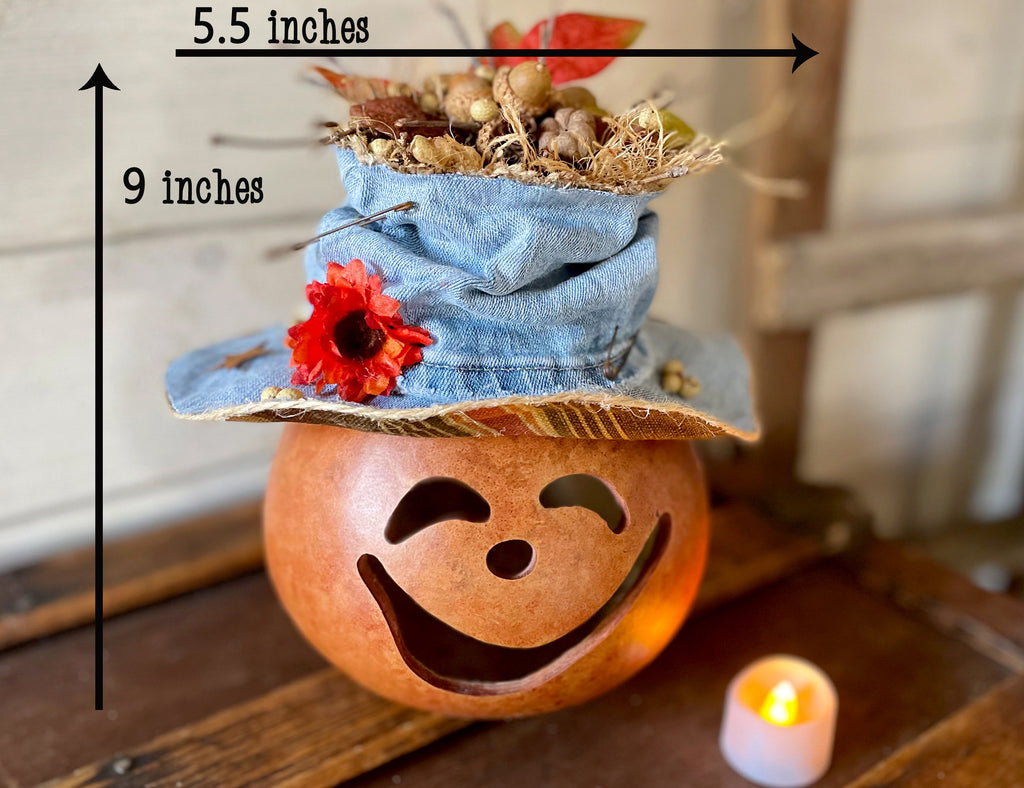 Decorative pumpkin with a face and denim hat on a wooden surface, with measurements indicated.