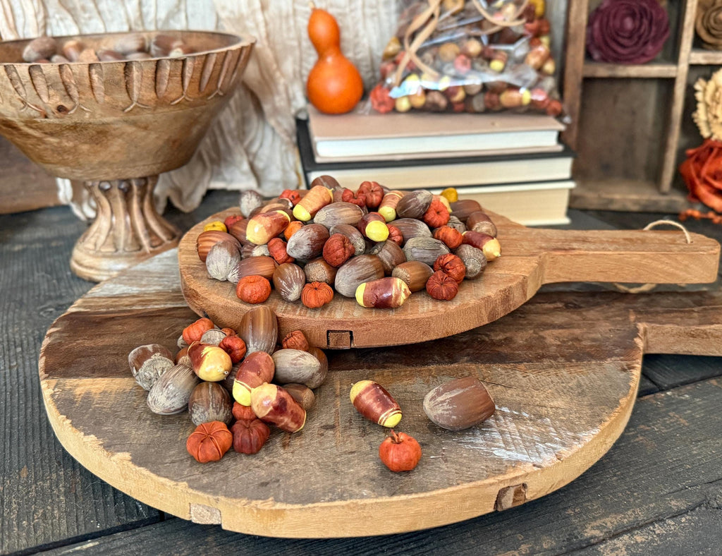 Wooden cutting board with assorted nuts, pumpkin pods, and primitive candy corn decorative items on a rustic settings