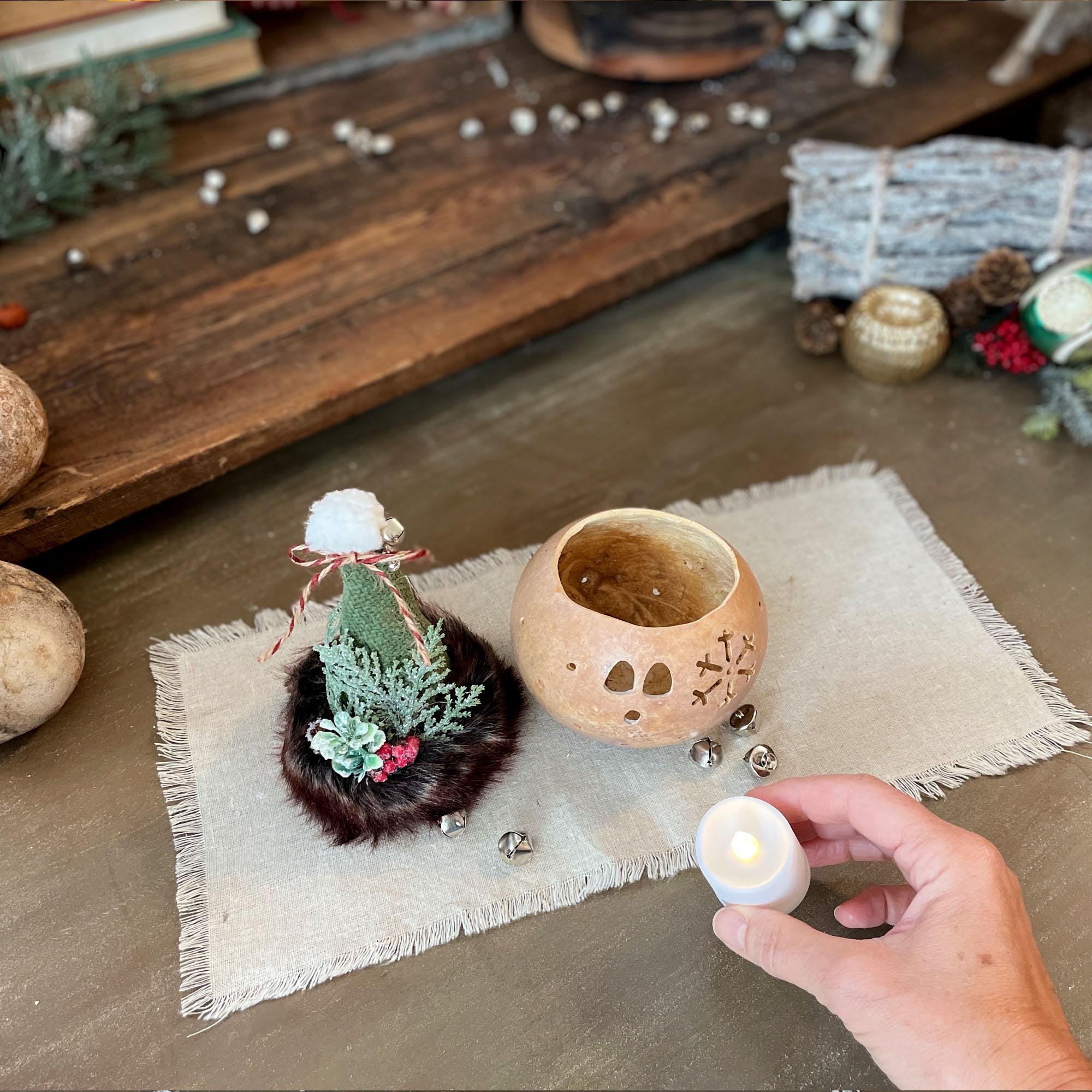 Decorative items on a wooden surface with a hand holding a small candle.