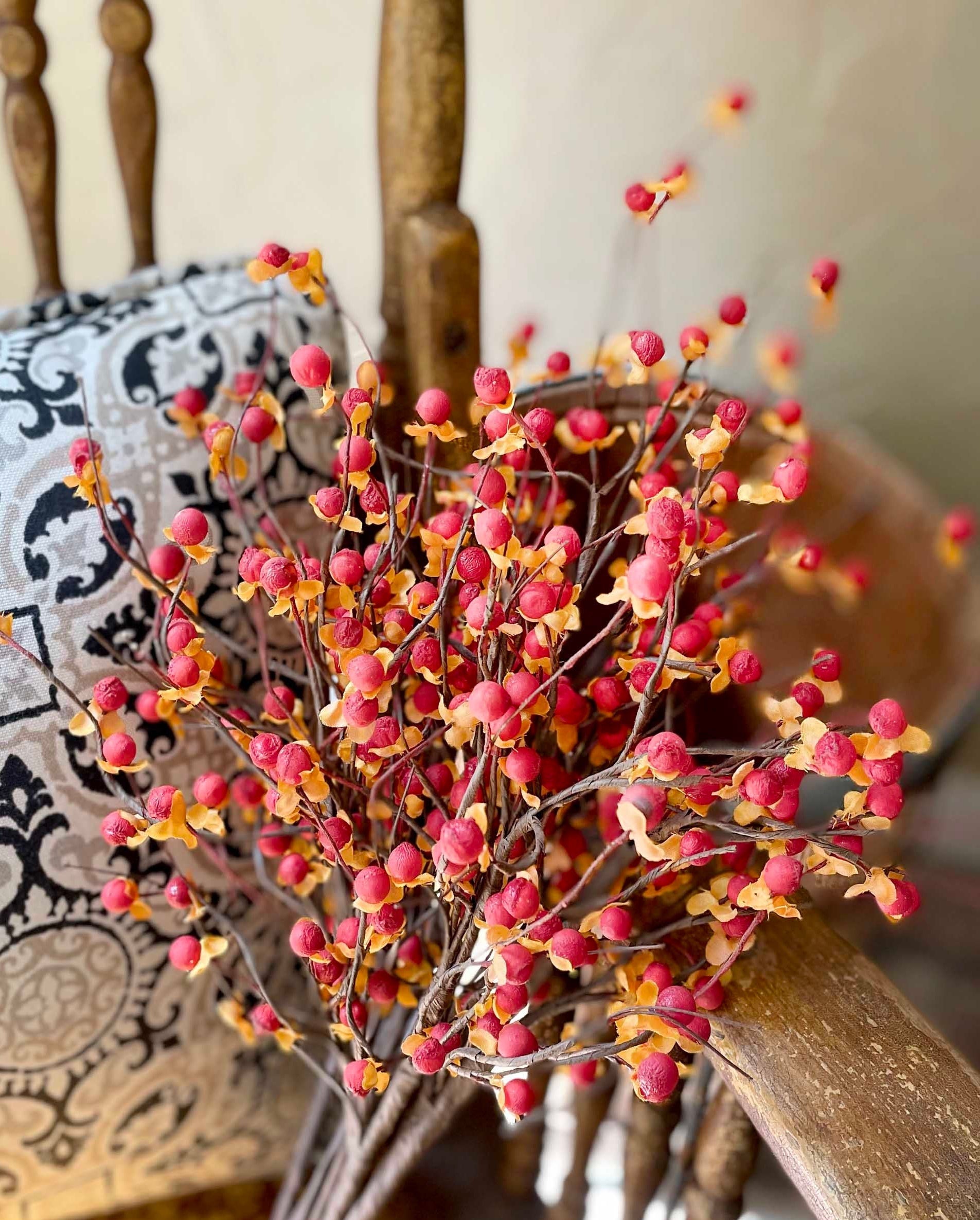 Decorative arrangement of red and orange berries on a wooden chair with a patterned cushion.