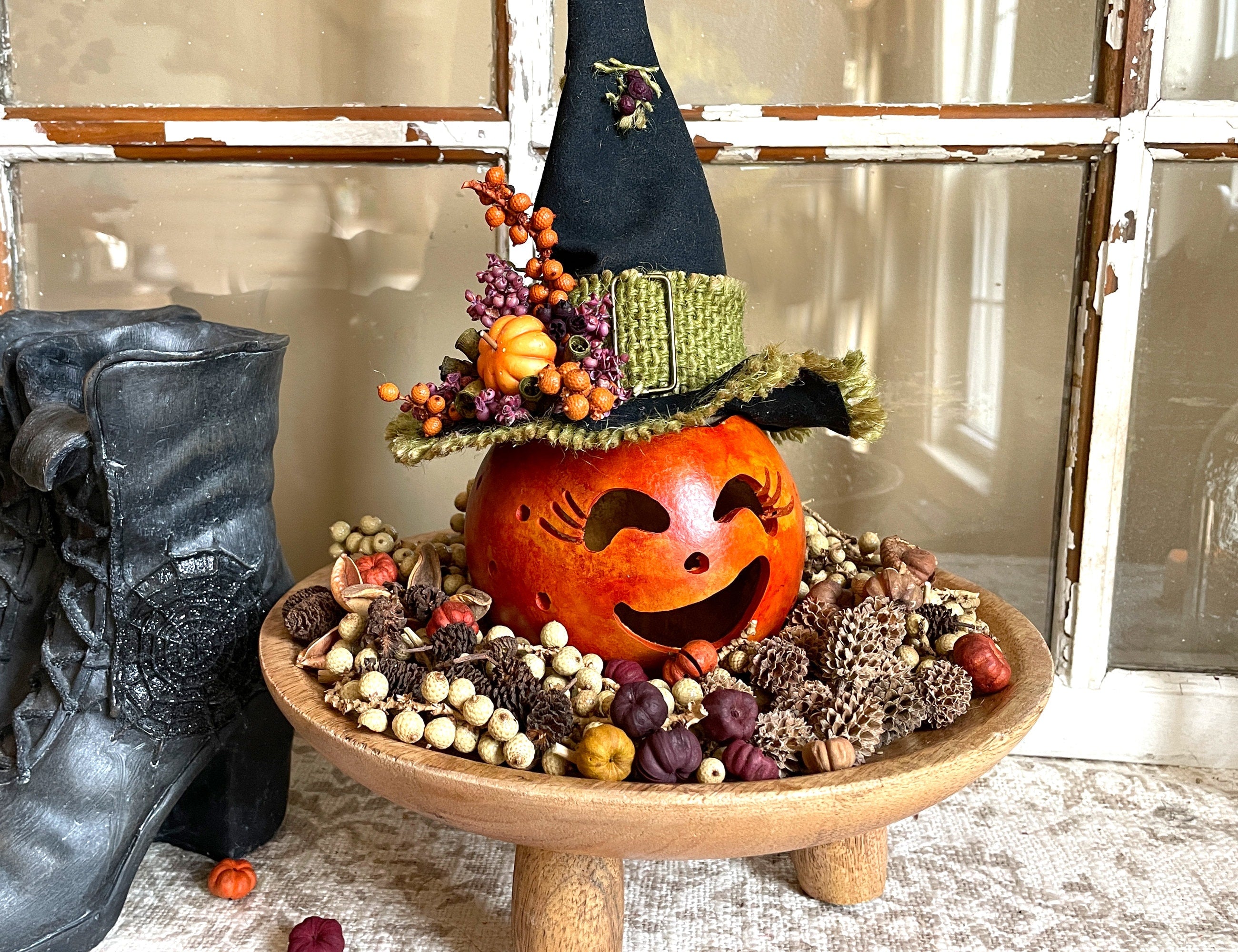 Decorative Halloween display with a carved pumpkin, pinecones, and berries on a wooden stand.