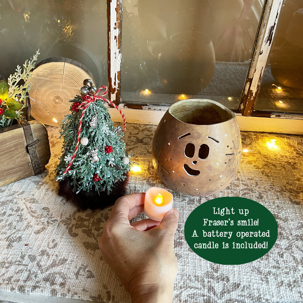 Decorative setup with a small Christmas tree, ceramic face pot, and battery-operated candle on a textured surface.