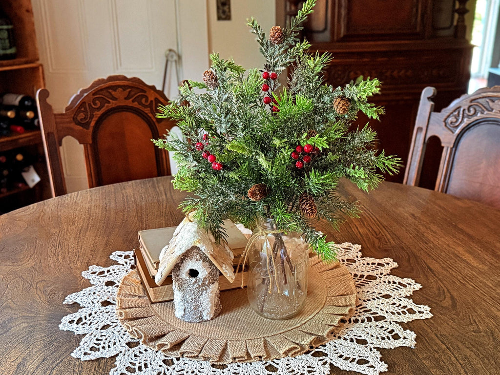 Decorative arrangement with greenery, berries, and a small birdhouse on a wooden table.