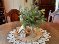 Decorative arrangement with greenery, berries, and a small birdhouse on a wooden table.