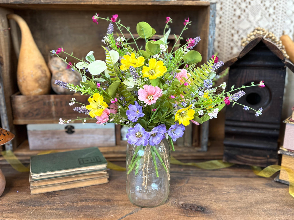 Bouquet of colorful flowers in a glass jar on a wooden surface with rustic decor.