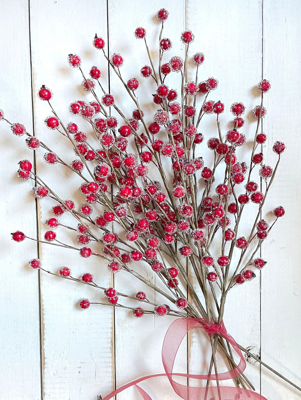 Decorative arrangement of red berries with a pink ribbon on a white wooden background