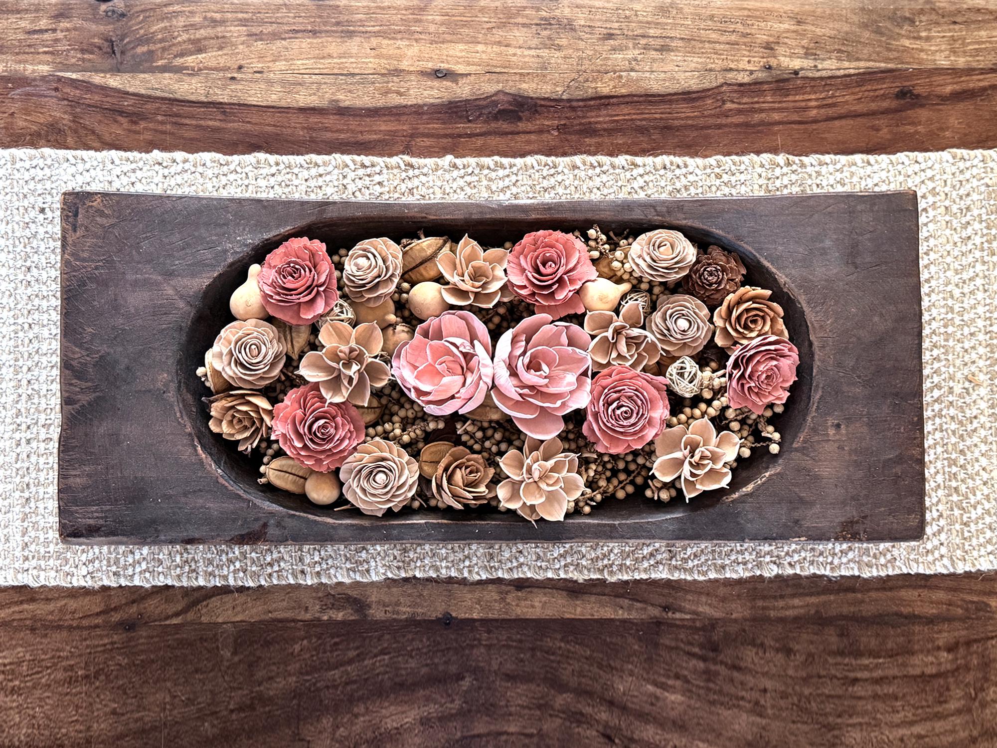 Decorative wooden tray with pink and beige floral arrangement on a wooden surface.