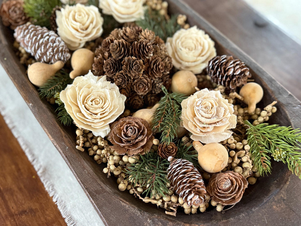 Decorative arrangement of flowers, pinecones, and berries in a wooden container.