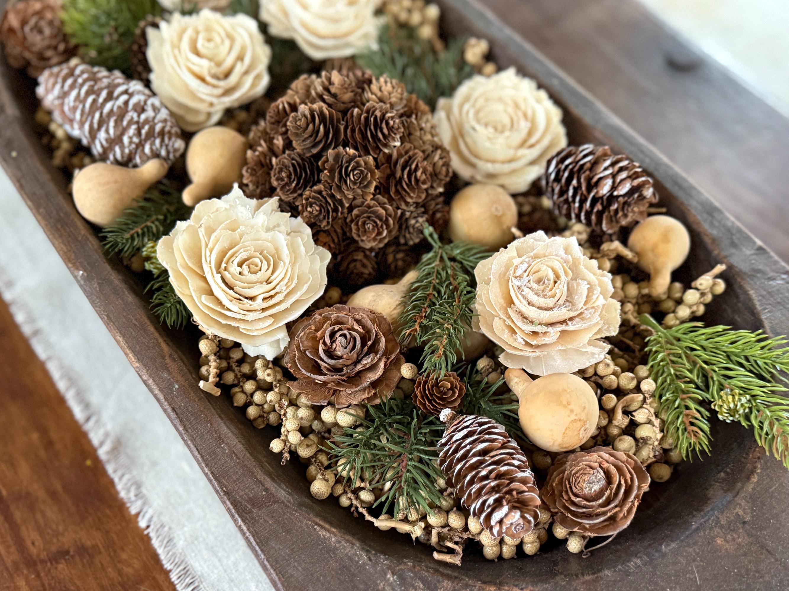 Decorative arrangement of flowers, pinecones, and berries in a wooden container.