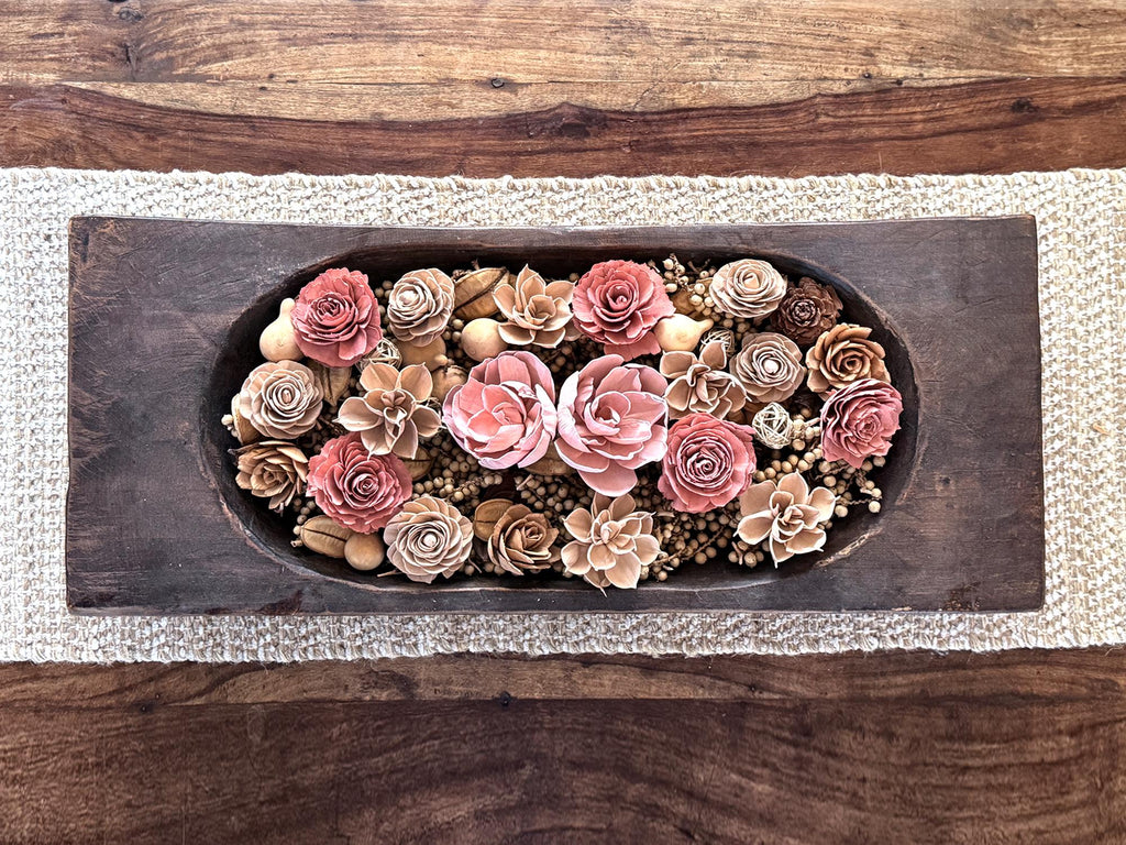 Decorative wooden dough bowl with neutral pink and beige floral arrangement on a coffee table