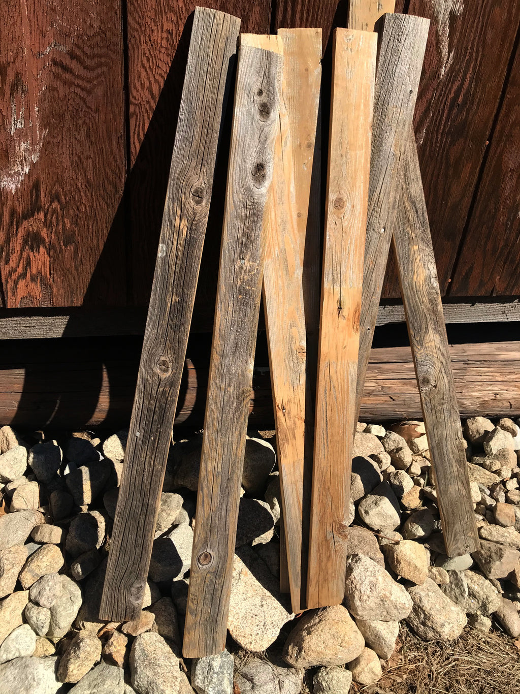 Stack of wooden planks against a wooden wall with stones at the base