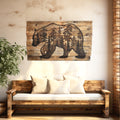 Wooden wall art of a bear with trees on a rustic wall above a wooden bench with white cushions.
