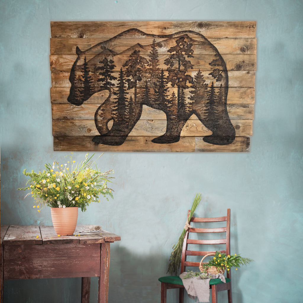Wooden wall art of a bear with trees on a blue wall above a rustic table and chair.