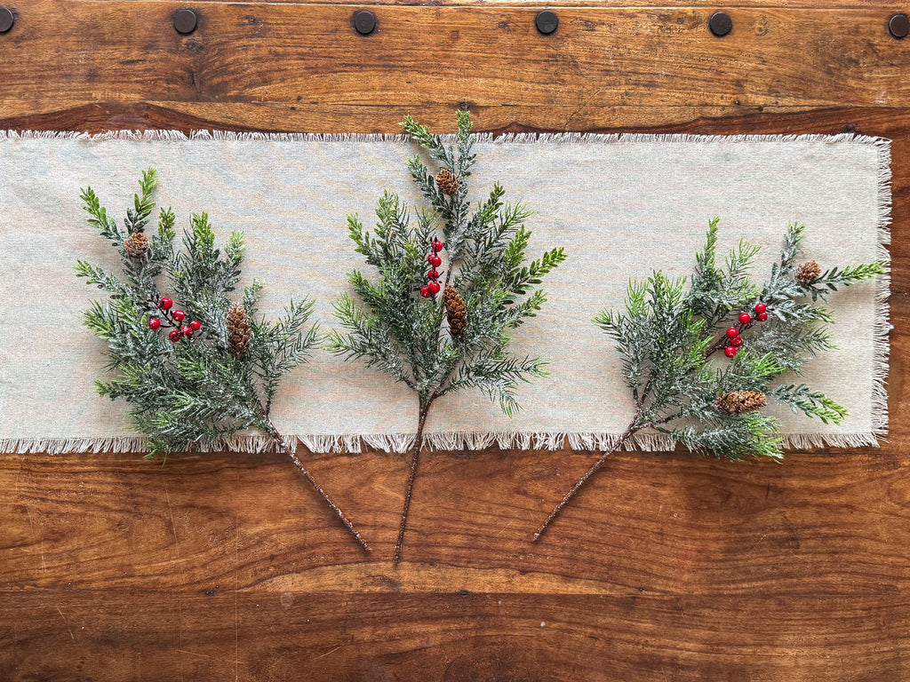Decorative greenery with red berries on a textured fabric runner over a wooden surface