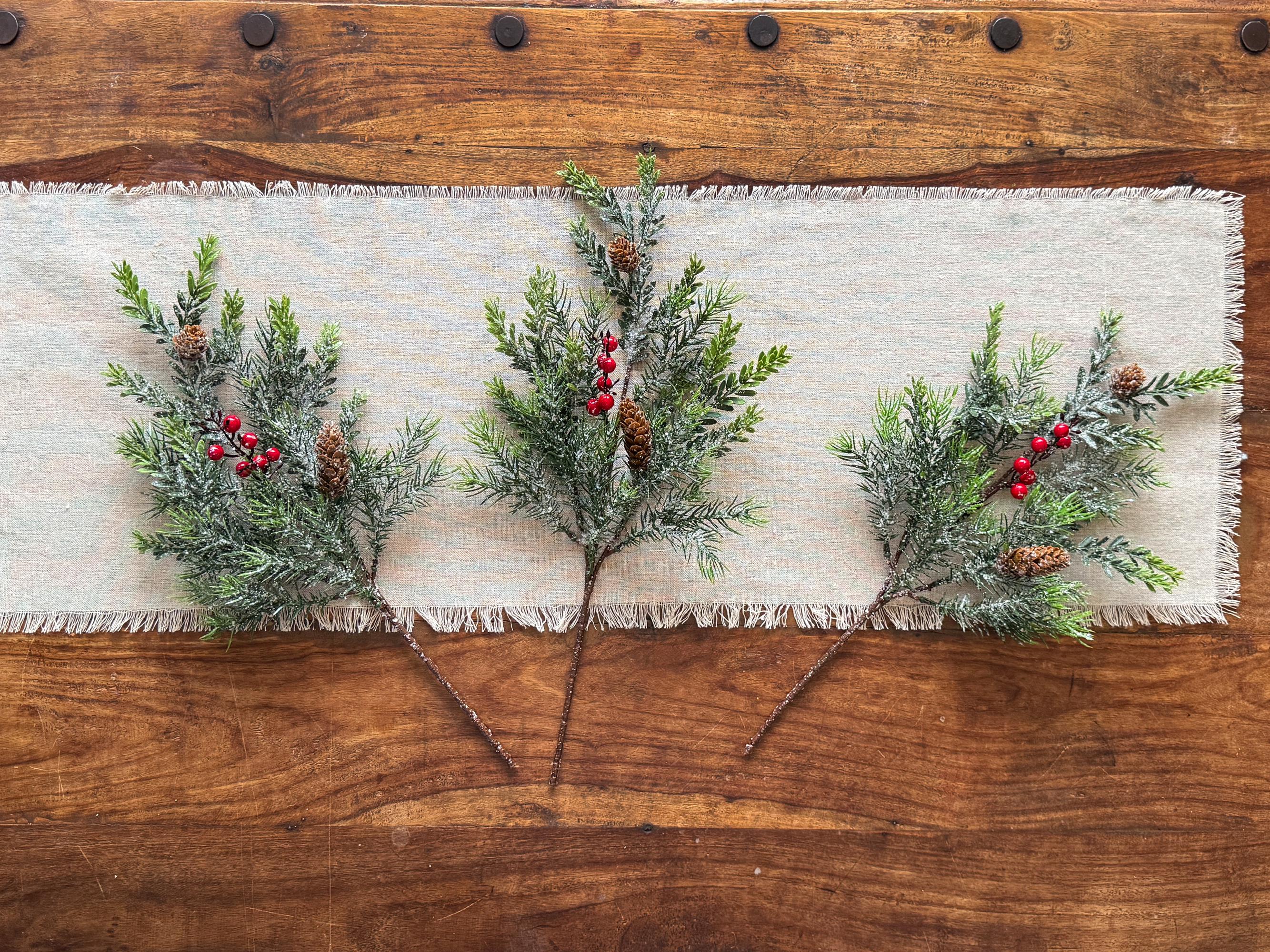 Decorative greenery with red berries on a textured fabric runner over a wooden surface