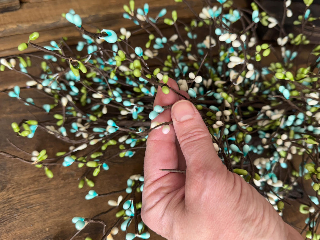 Hand holding a branch with turquoise and green leaves against a wooden background
