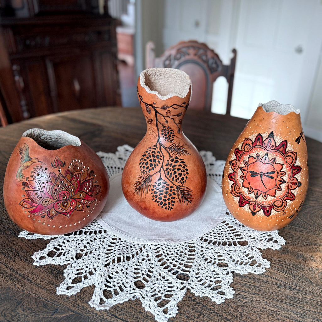 Three ornately carved gourds on a lace doily with a wooden table and chair in the background.