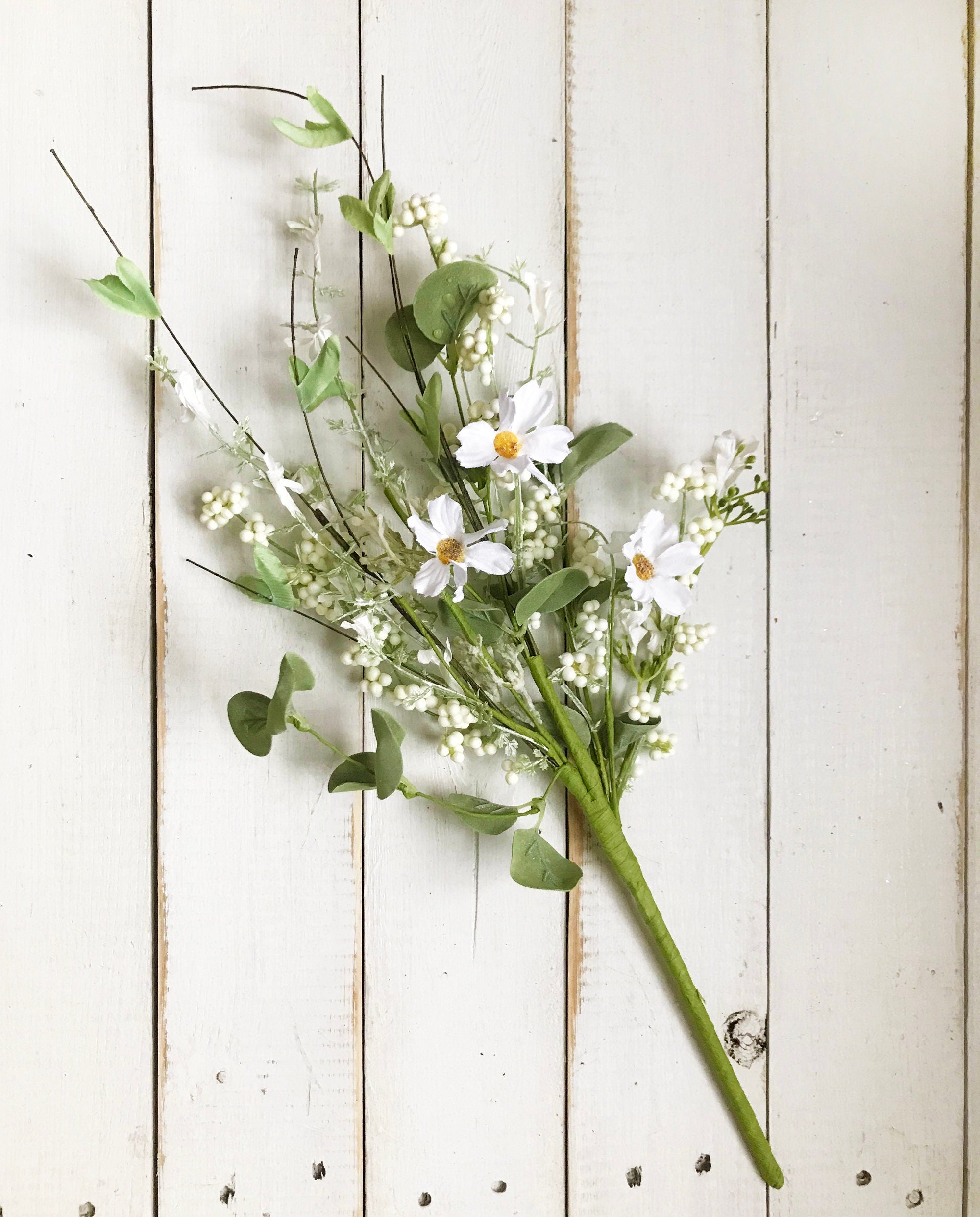 Bouquet of white flowers with green leaves on a light wooden background