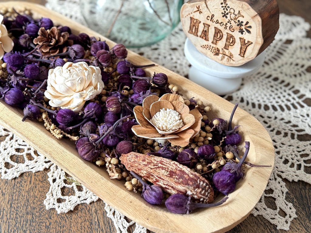 Decorative arrangement of dried flowers and herbs in a wooden dough bowl on a lace doily.