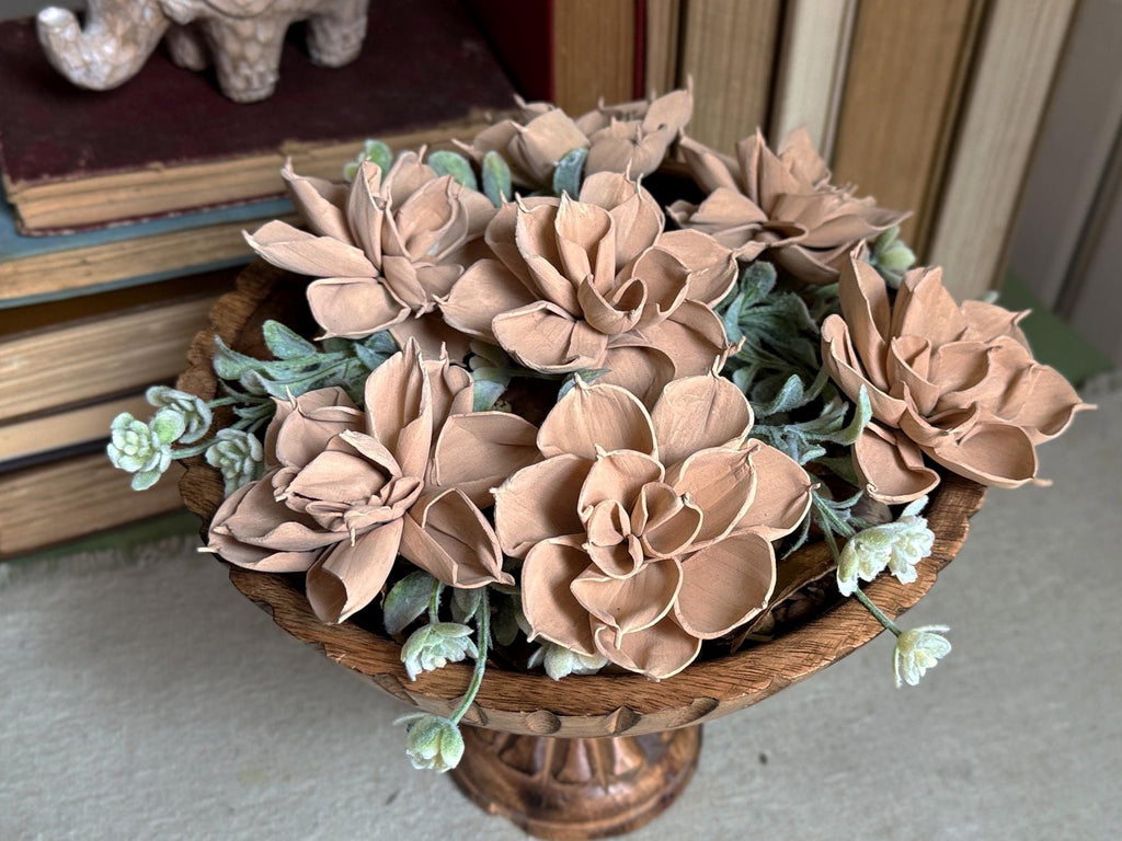 Decorative flower arrangement in a wooden vase on a surface with books in the background.