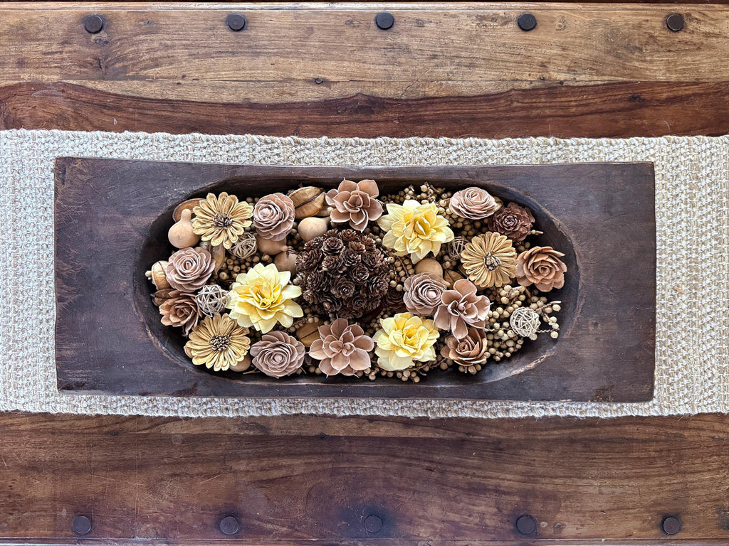Decorative arrangement of flowers and pinecones in a wooden bowl on a wooden surface.