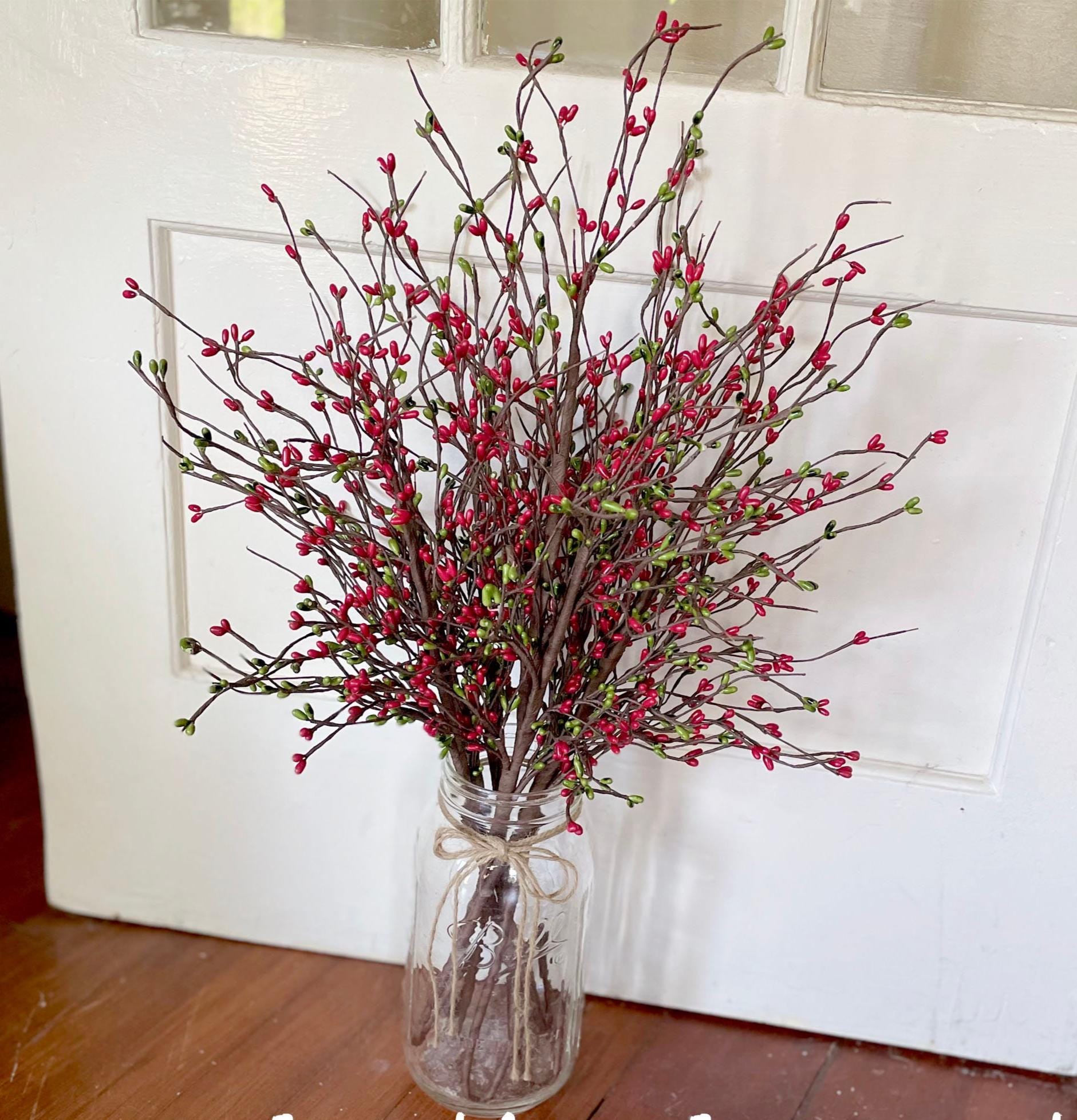 Bouquet of red and green branches in a clear glass vase on a wooden floor.