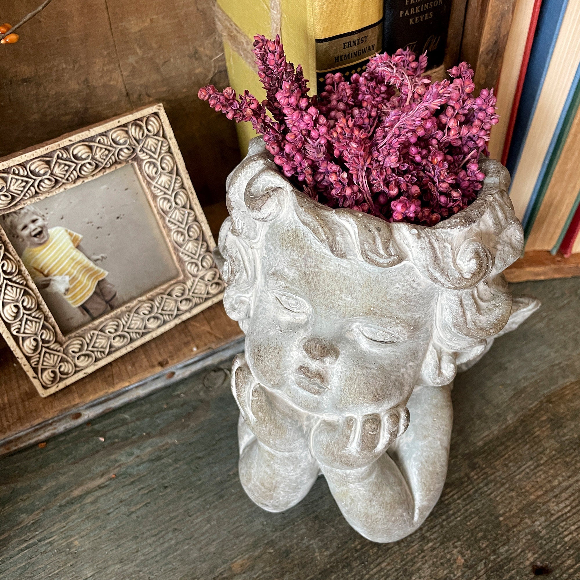 Decorative stone face planter with pink flowers on a wooden surface
