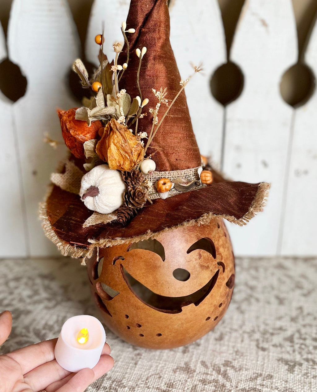 Decorative pumpkin with witch hat and carved face, held by a hand with a lit candle.