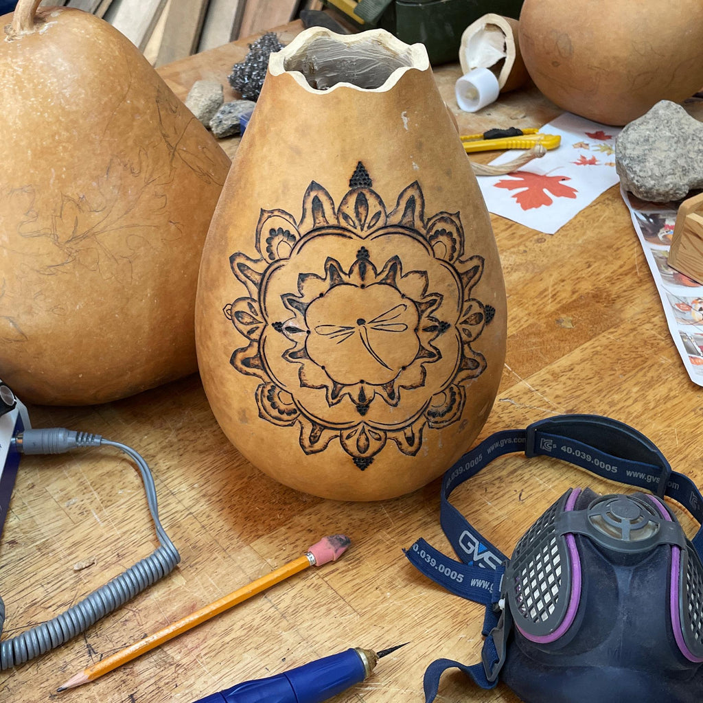 Carved gourd with mandala design on a wooden table with tools and a mask.