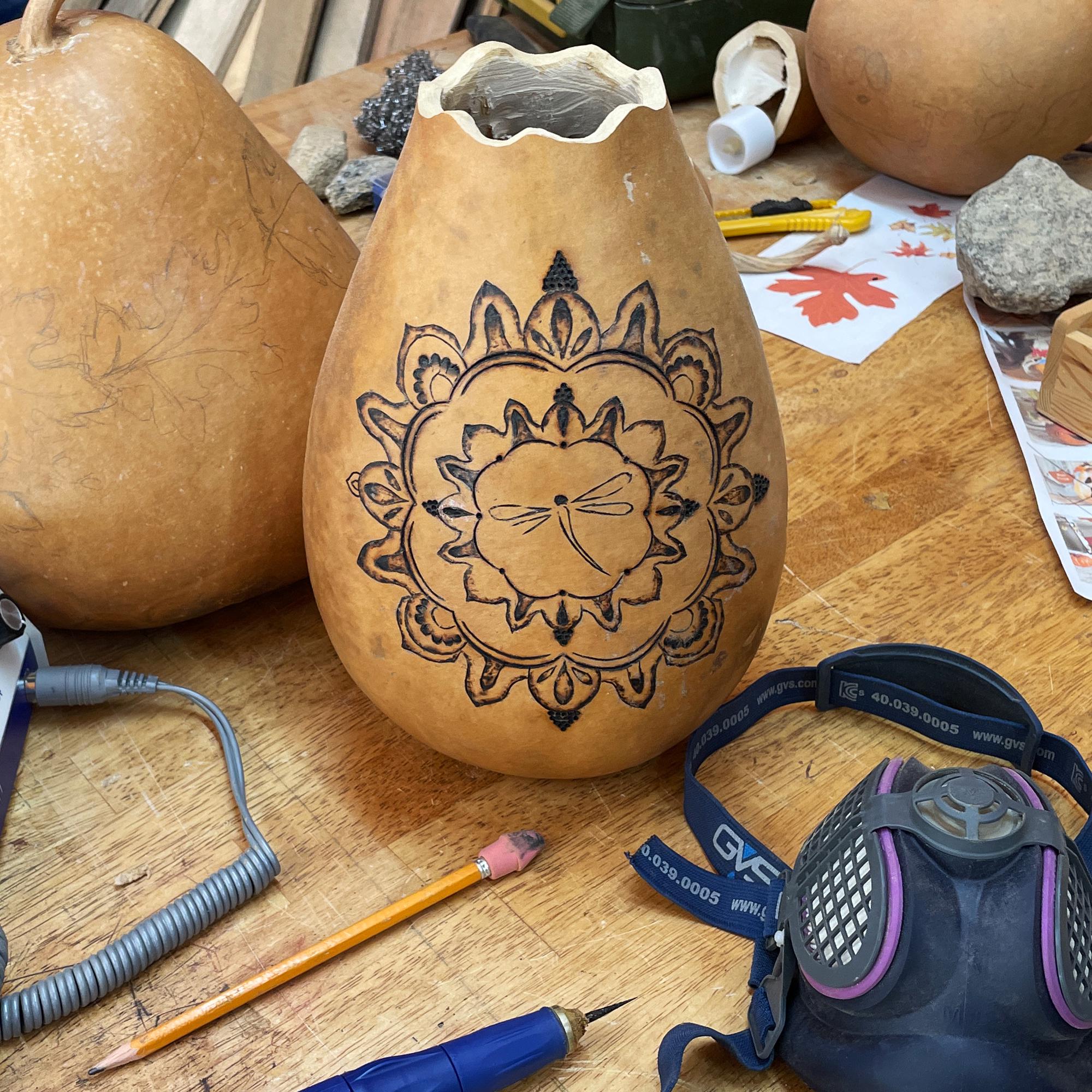 Carved gourd with mandala design on a wooden table with tools and a mask.