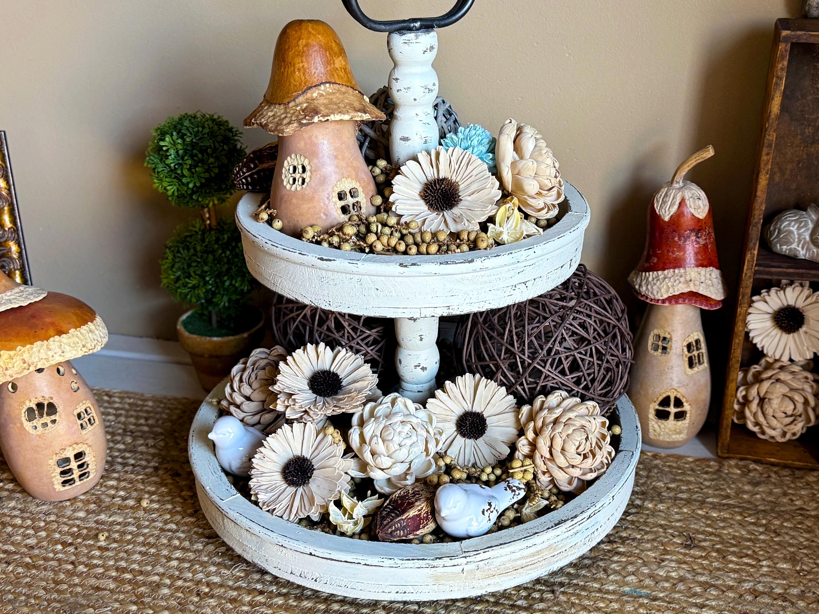Decorative tiered stand with small houses, flowers, and decorative items on a textured surface.