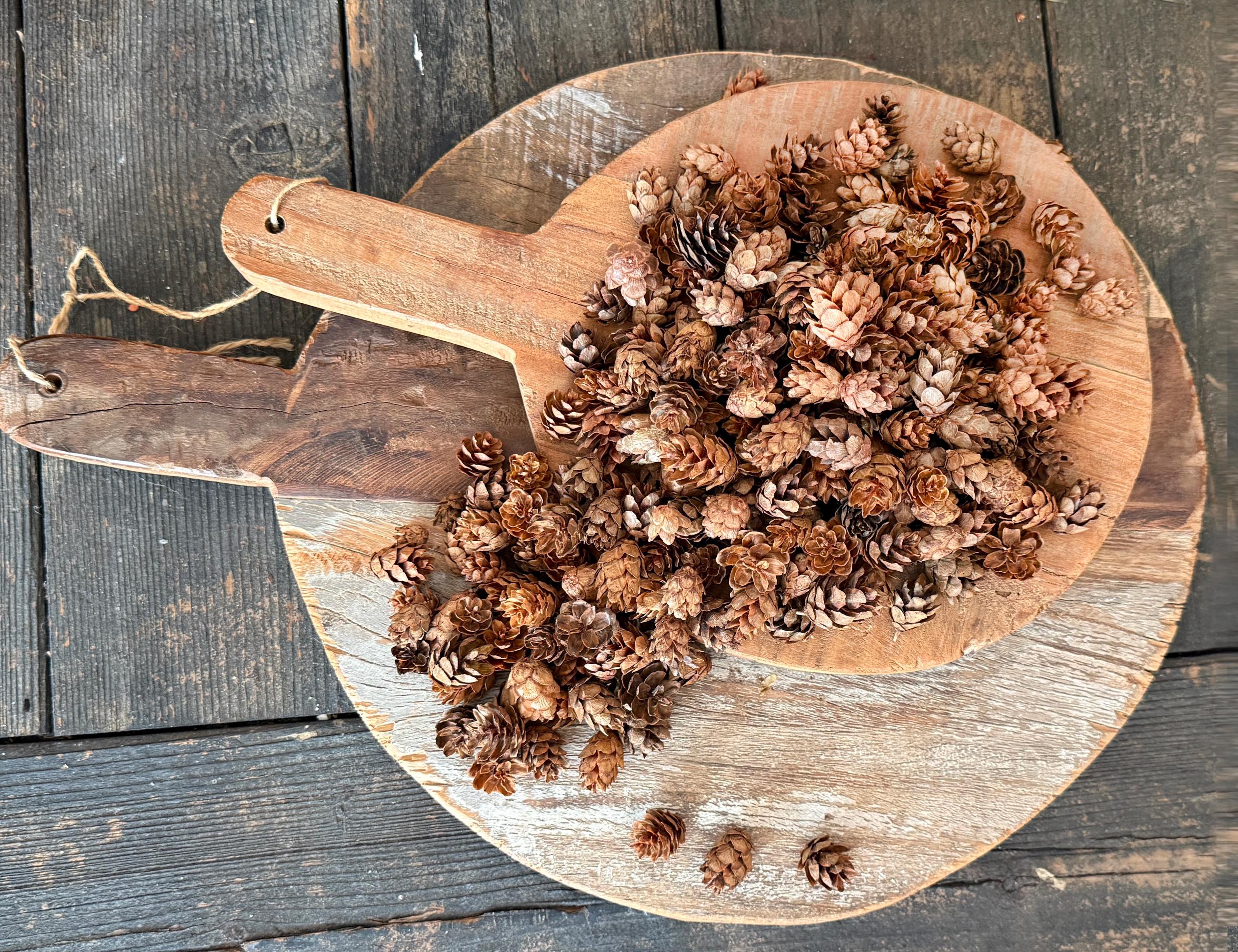 Wooden spoon filled with pine cones on a wooden surface