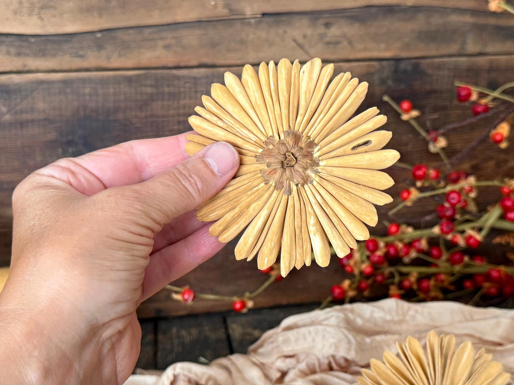 Hand holding a dried yellow flower against a rustic wooden background with red berries.