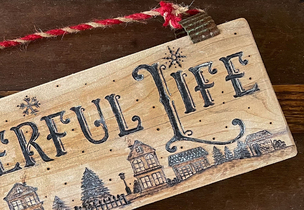 Wooden sign with 'Gleeful Life' text and decorative houses on a wooden background