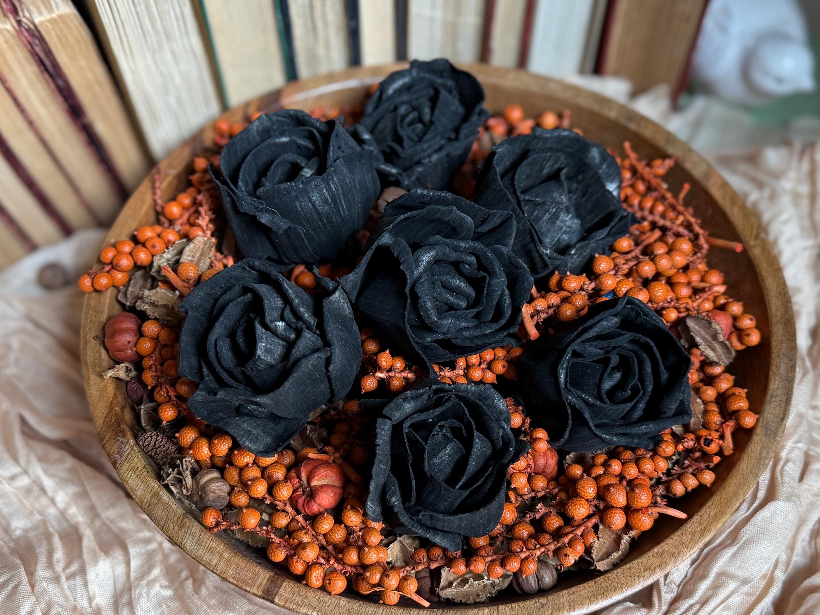 Black roses and orange berries on a wooden plate with books in the background