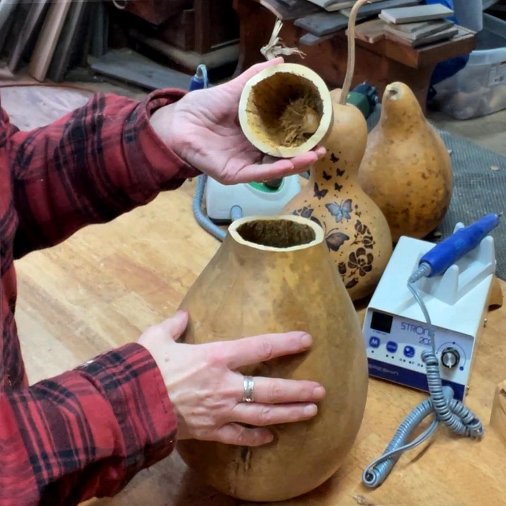 Person holding a gourd with another gourd inside, in a workshop setting.