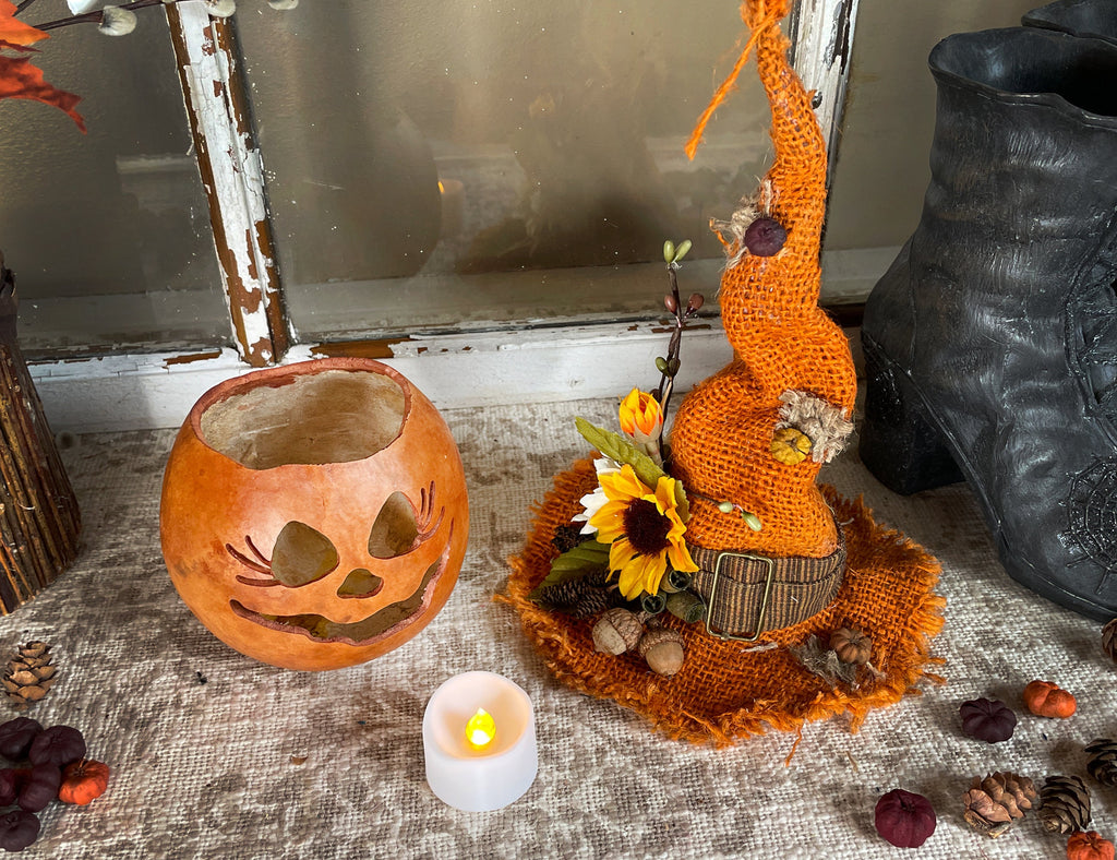 Decorative autumn scene with a crocheted pumpkin, carved pumpkin, and candle on a textured surface.
