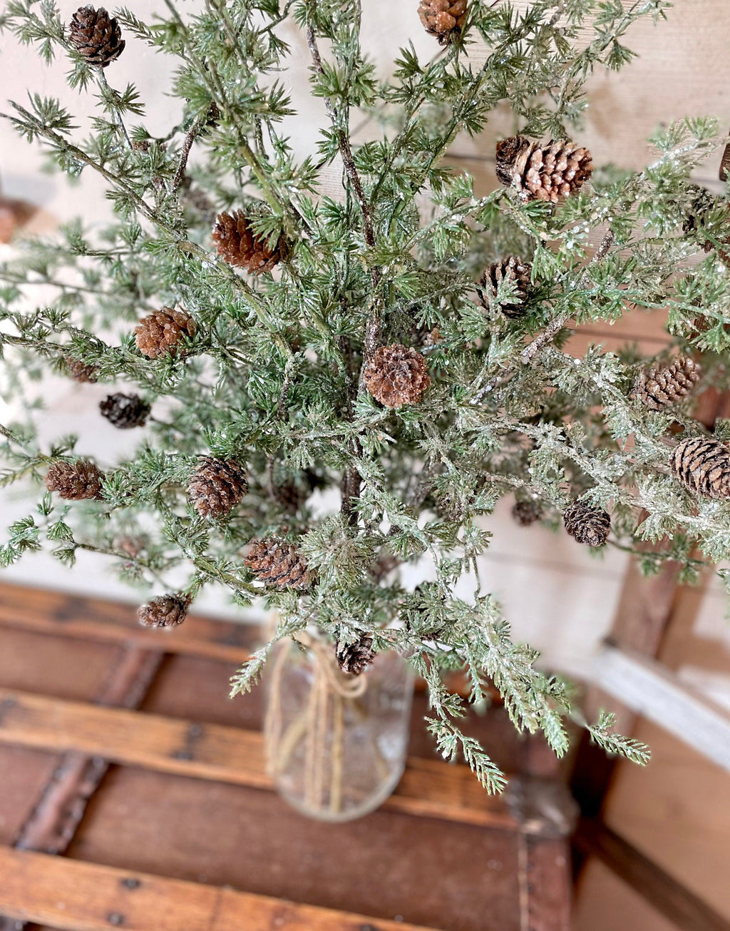 Decorative arrangement of greenery and pinecones in a clear vase on a wooden surface.