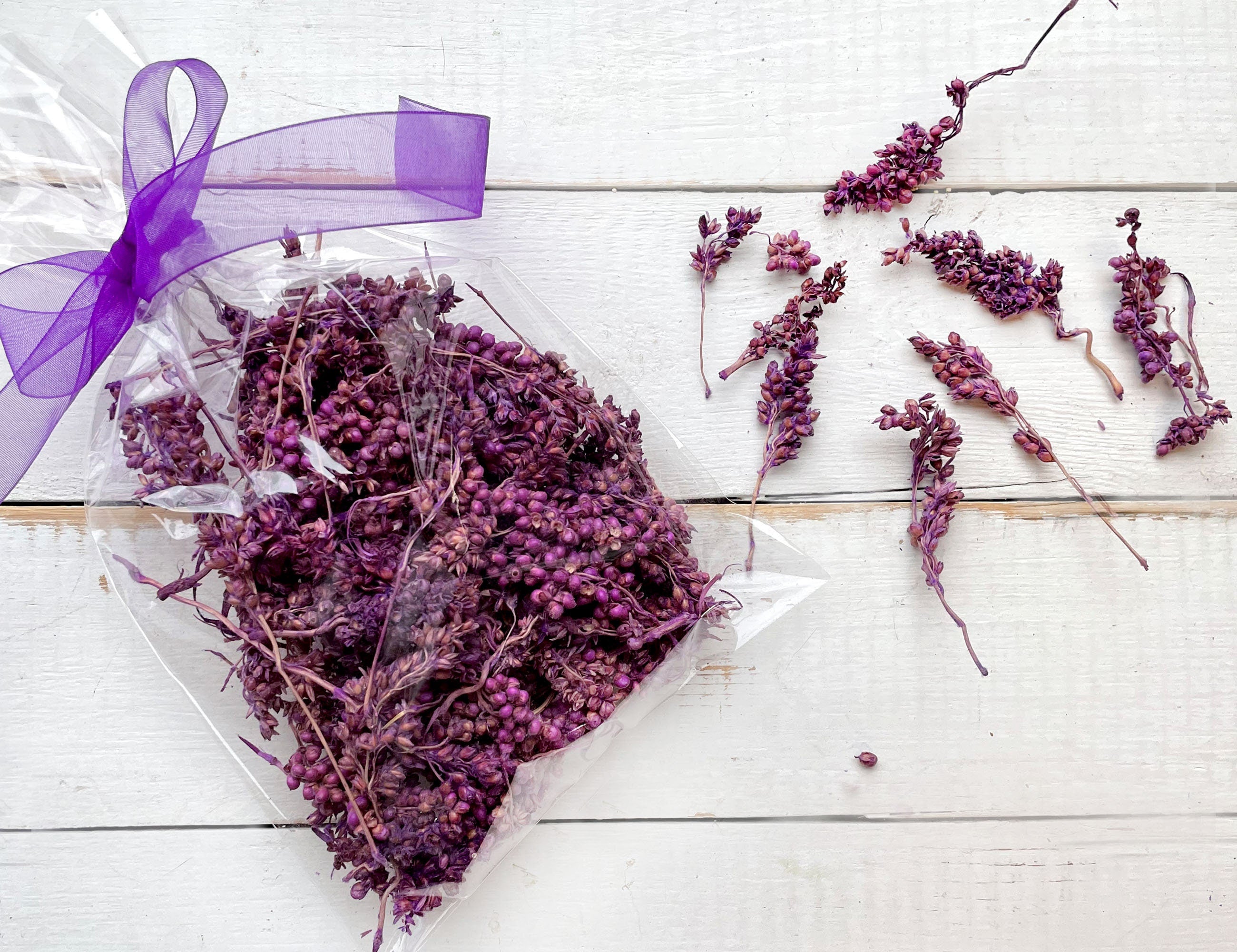 Dried purple flowers in a clear package with a purple ribbon on a white wooden surface.