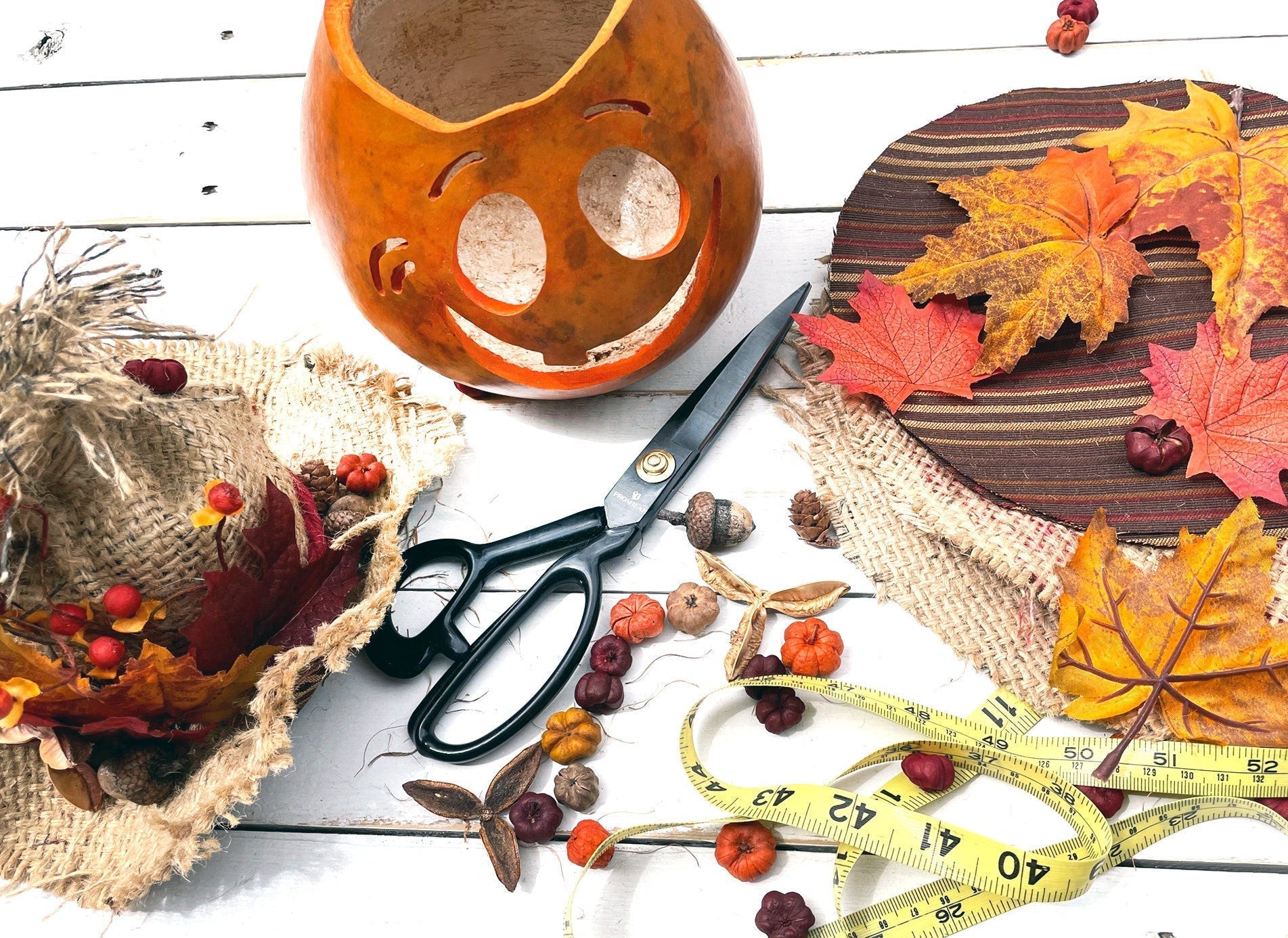 Autumn-themed decor items including a pumpkin, leaves, scissors, and a tape measure on a wooden surface.