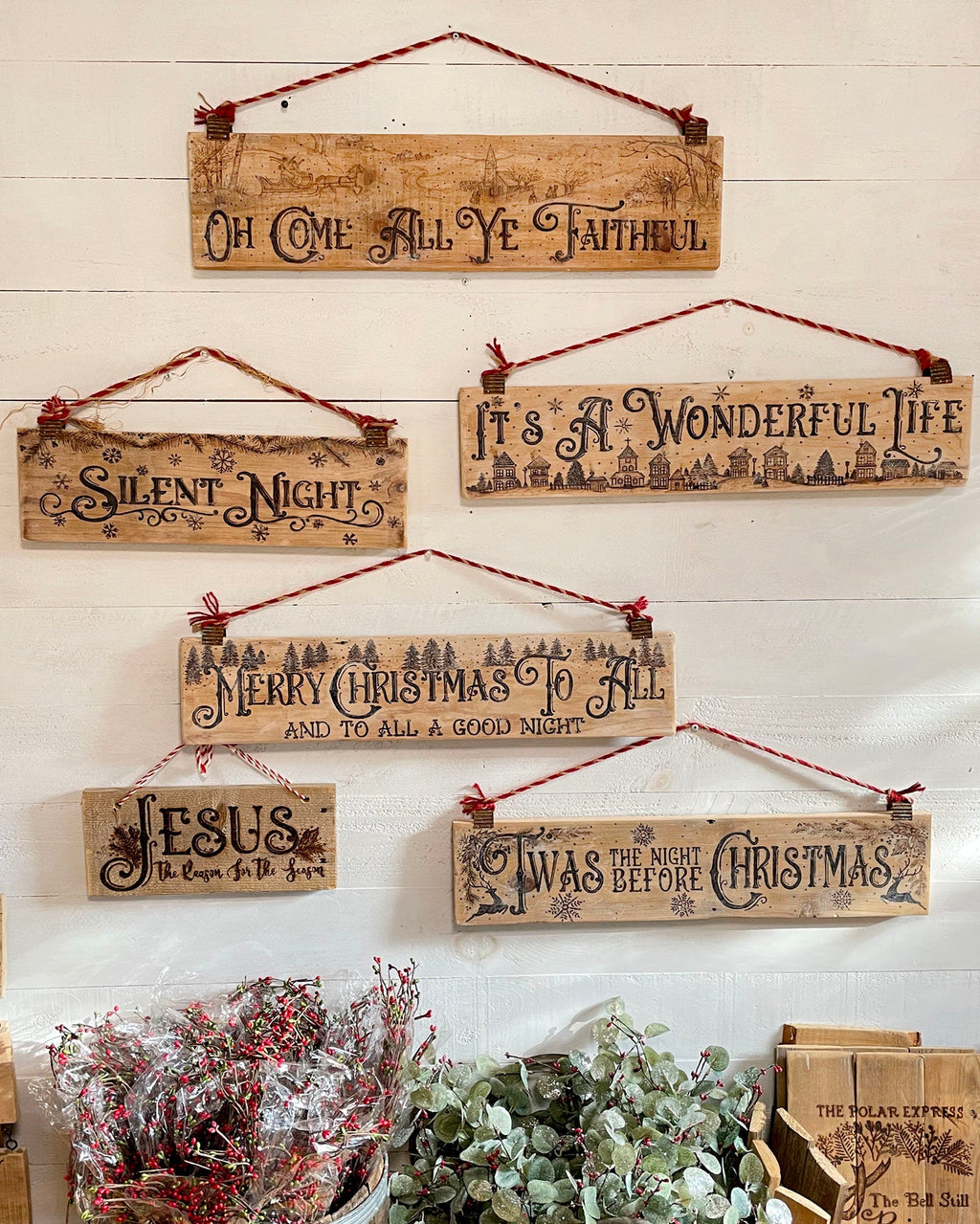 Set of wooden Christmas signs with festive phrases on a white wall.