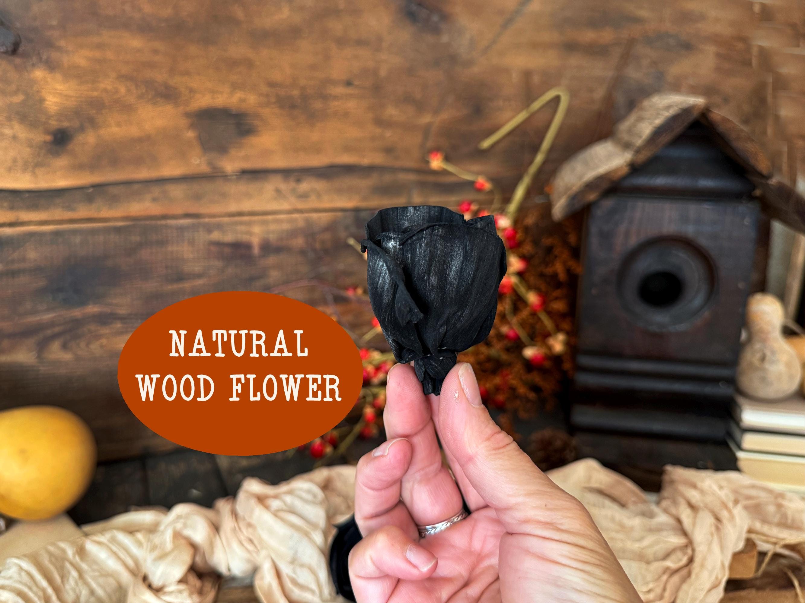 Hand holding a black decorative wood rose against a rustic wooden background with text 'Natural Wood Flower'.