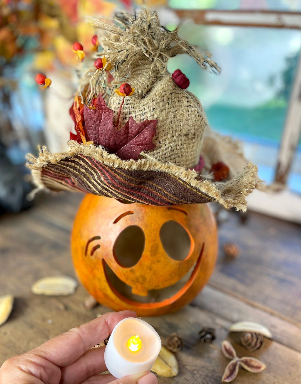 Decorative pumpkin with a face, straw hat, and autumn leaves on a wooden surface.