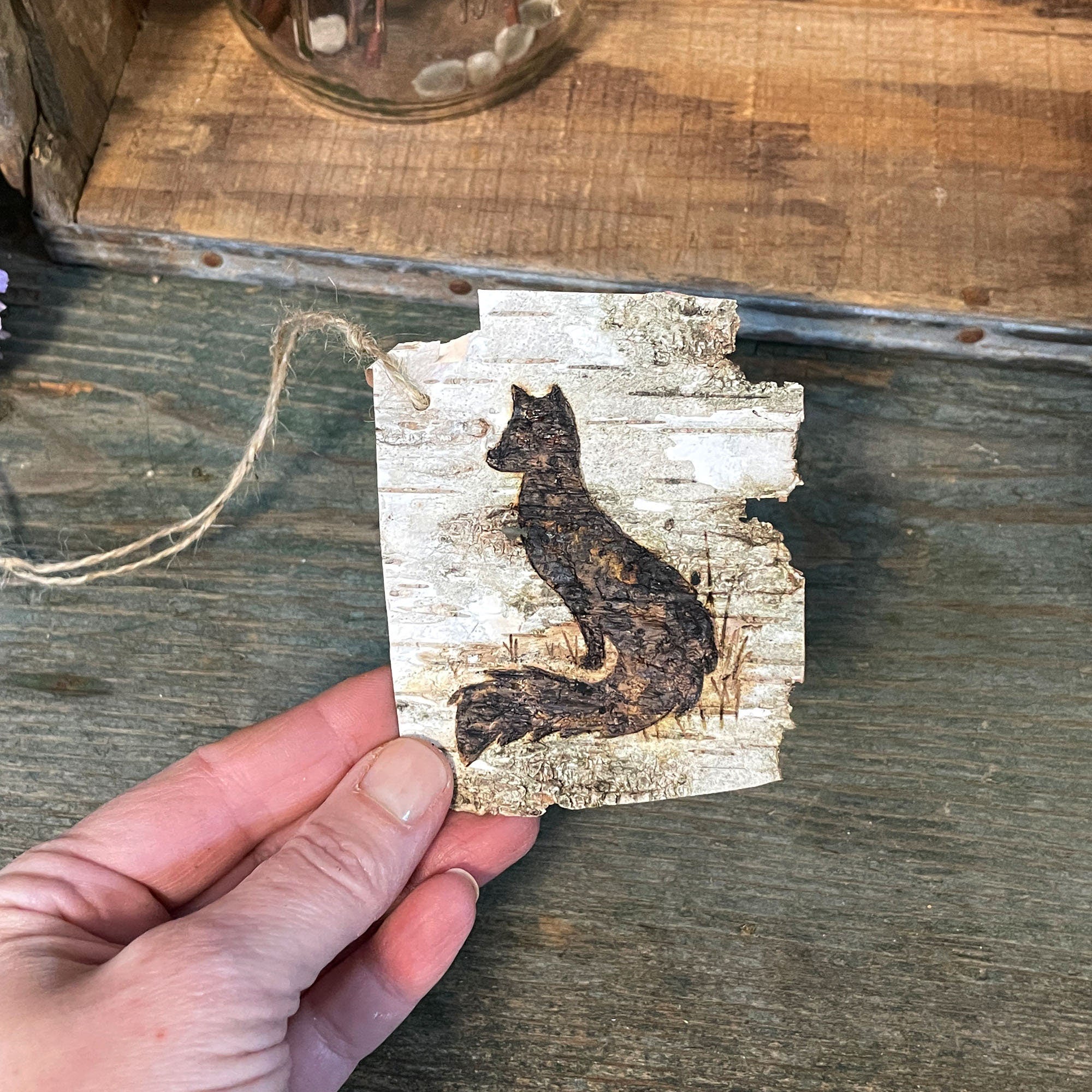 Hand holding a wooden ornament with a fox design on a rustic wooden surface