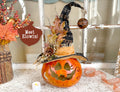Decorative pumpkin with a witch hat and autumn leaves on a table.