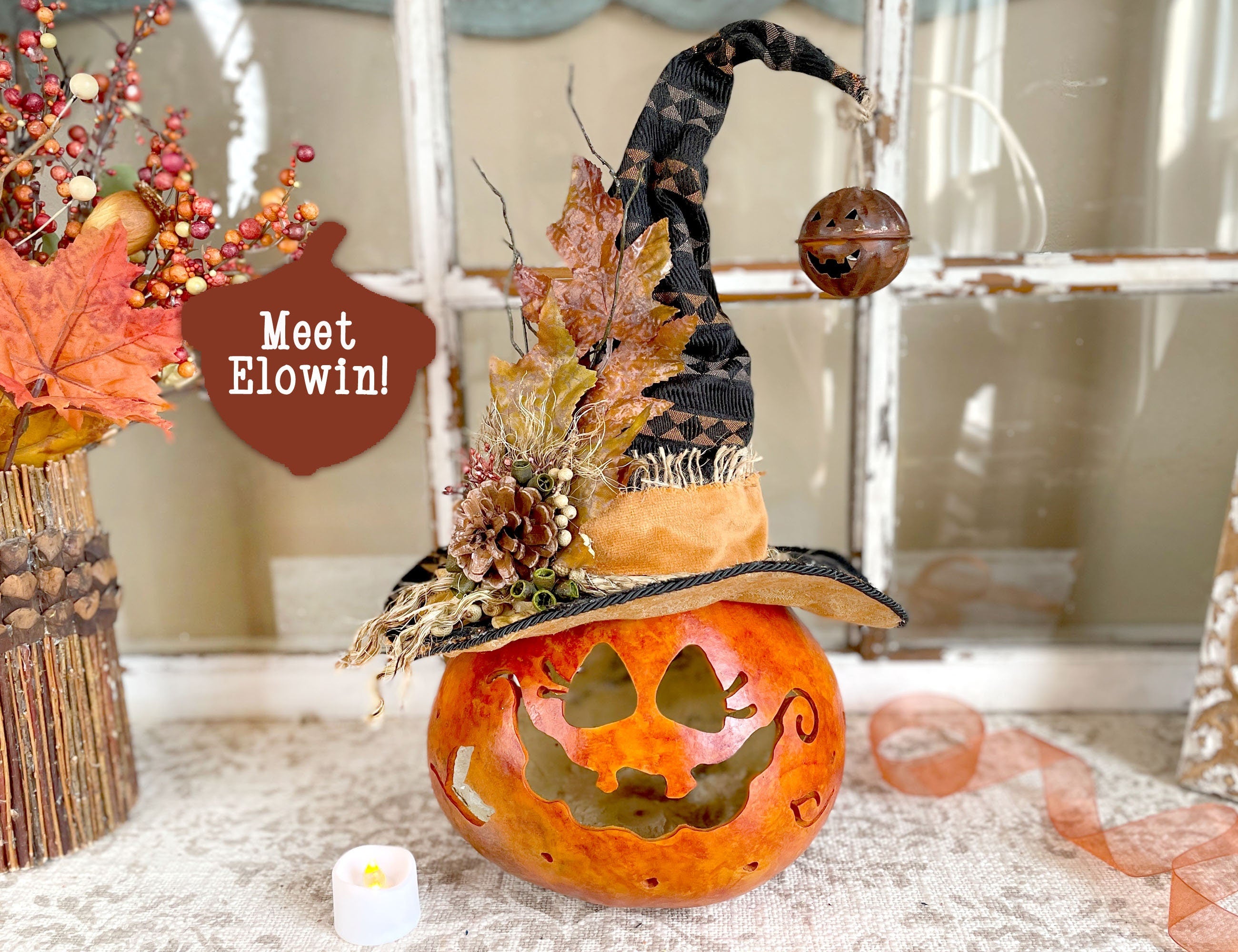 Decorative pumpkin with a witch hat and autumn leaves on a table.