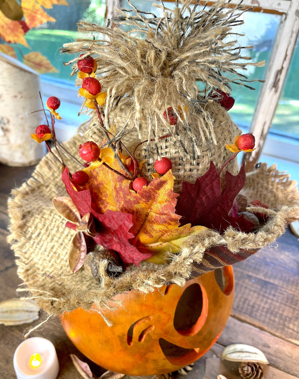 Decorative fall arrangement with pumpkins, leaves, and berries on a wooden surface.