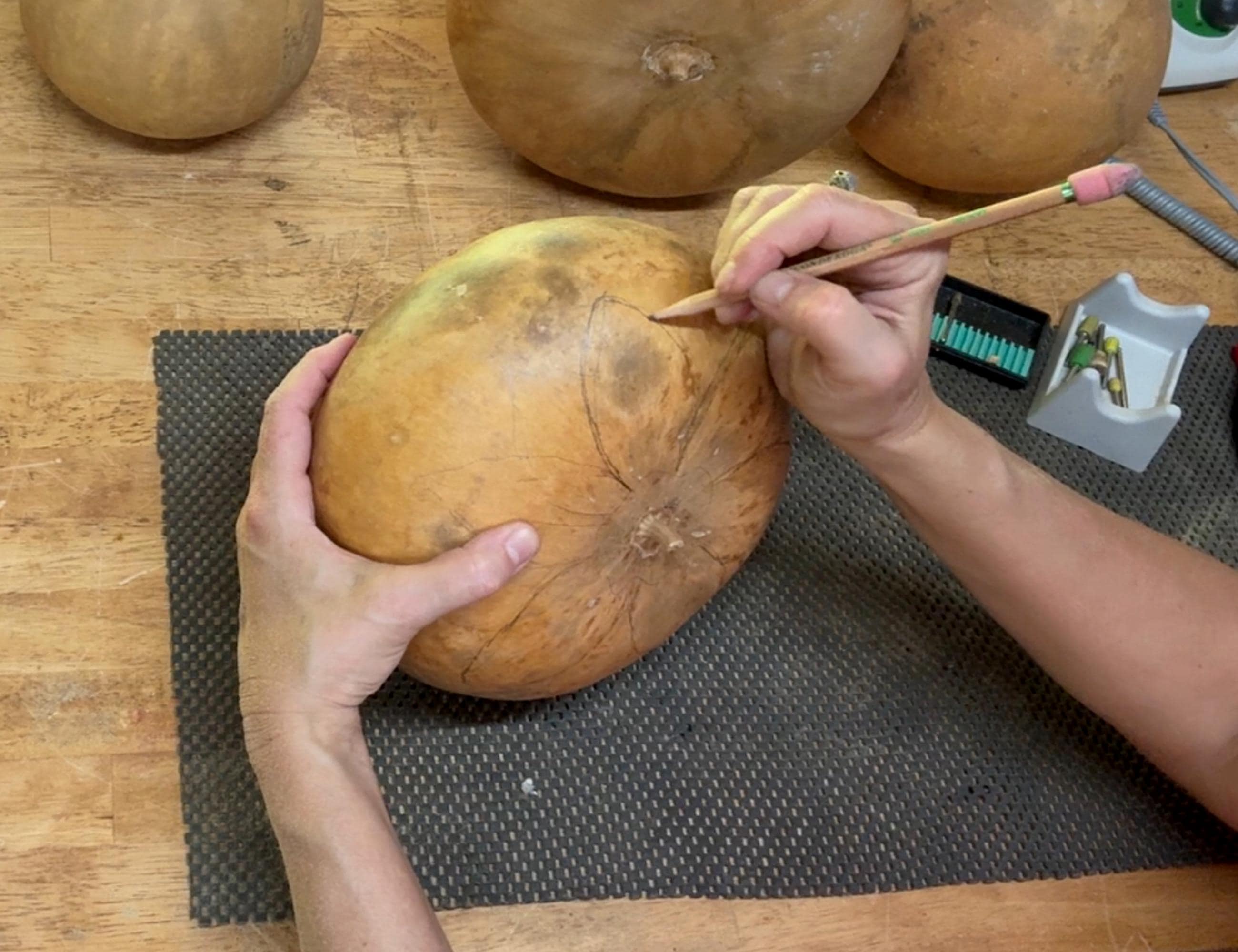Person carving a pumpkin on a wooden table with tools.