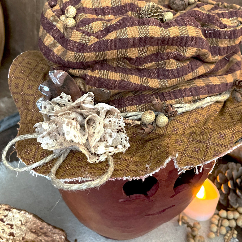 Decorative pumpkin with a plaid fabric hat and natural elements on a neutral background