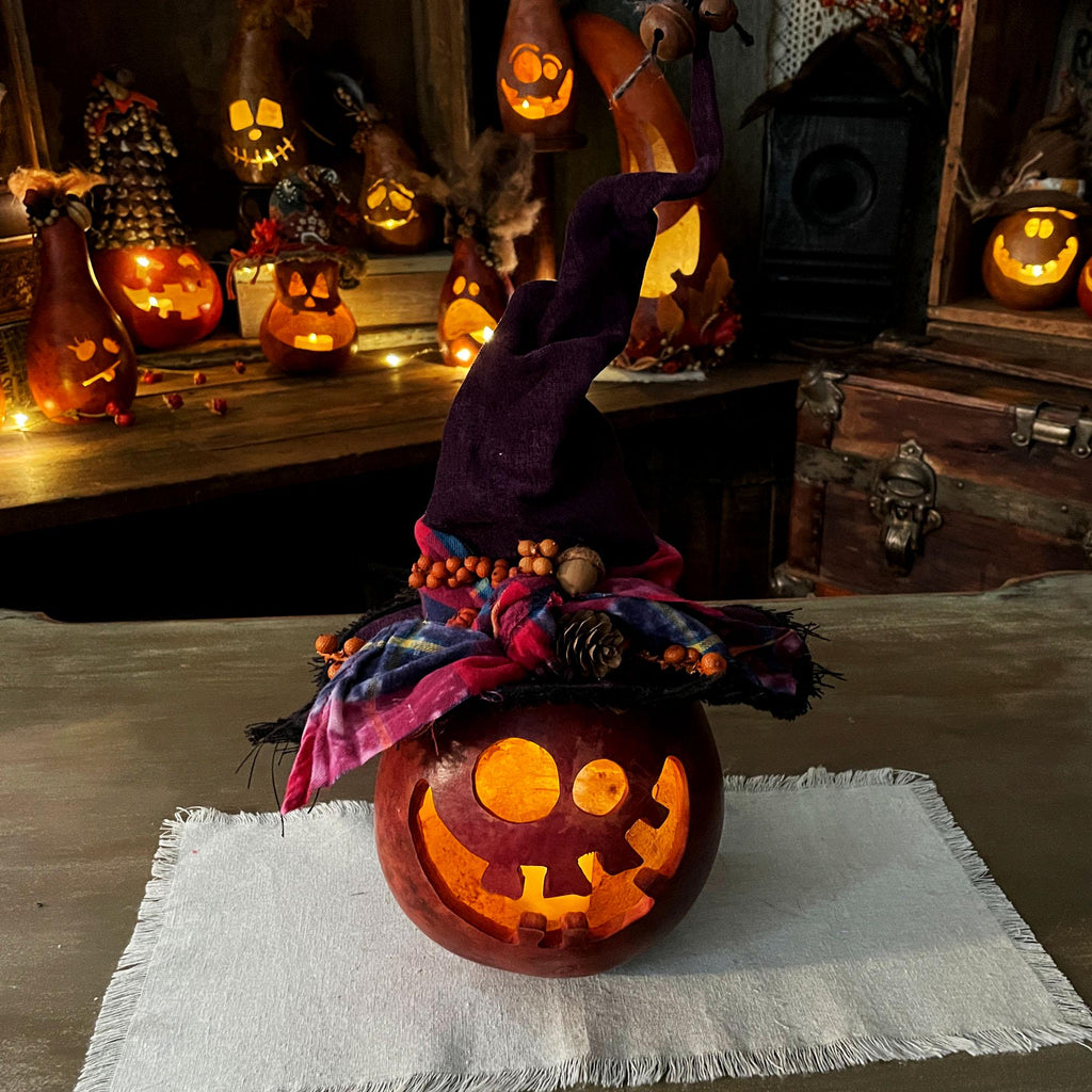 Decorative Halloween pumpkin with a witch hat on a tablecloth, surrounded by more pumpkins and decorations.